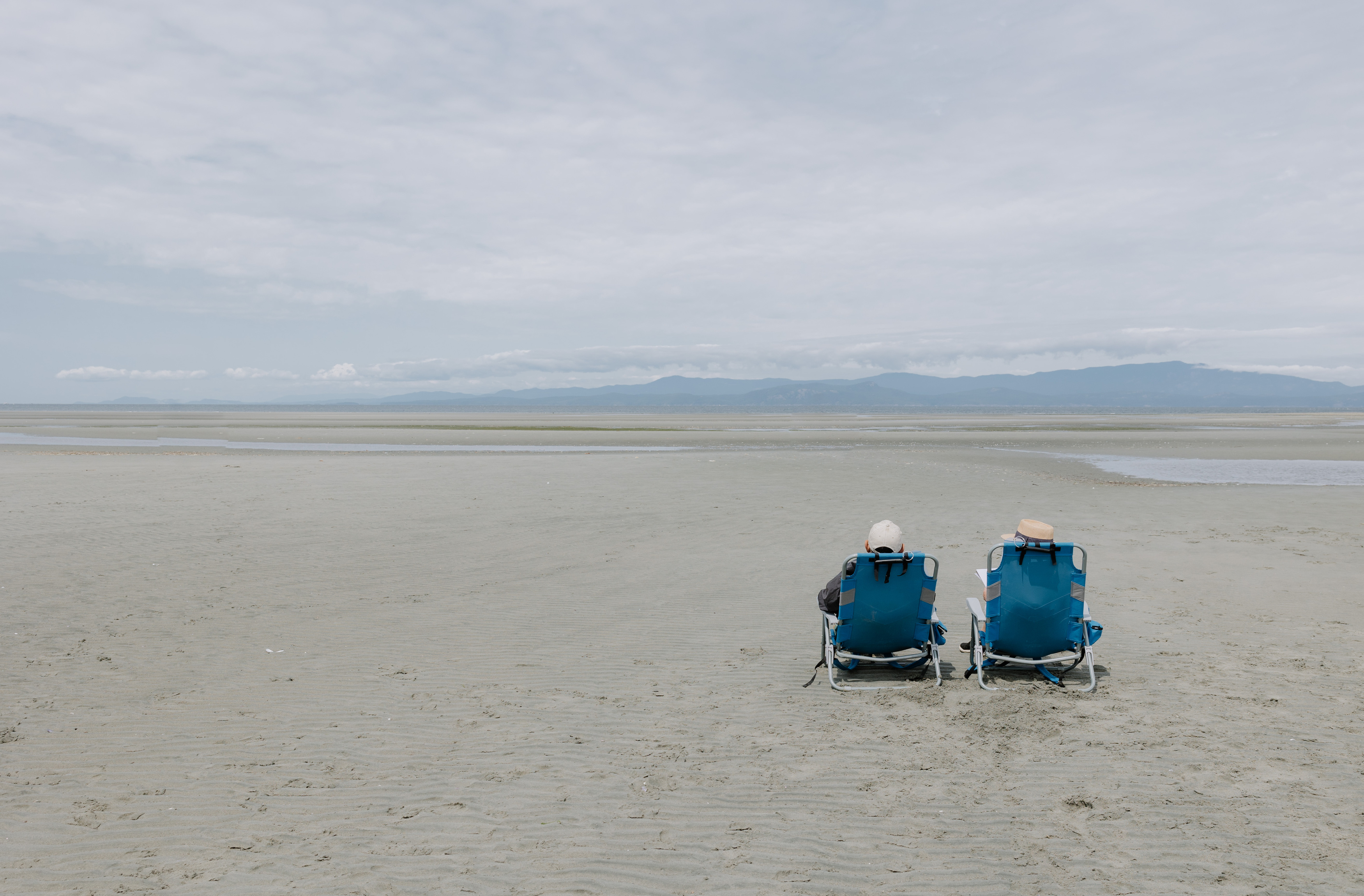 two people sitting in chairs on a beach