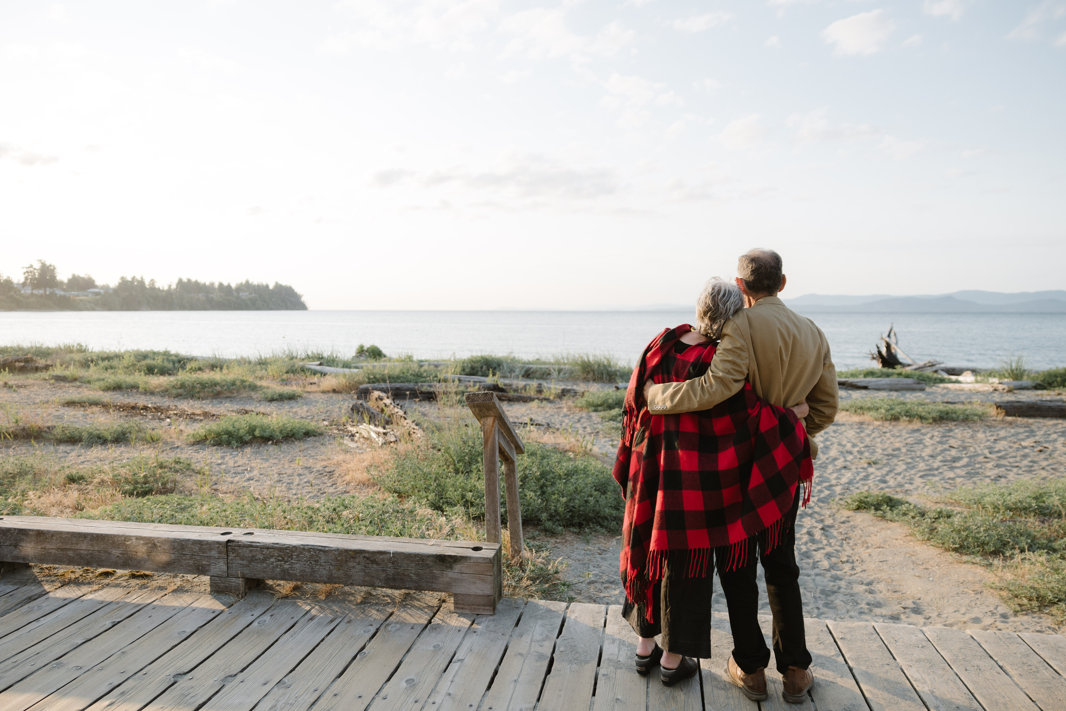 a man and woman standing on a wooden platform looking at the water